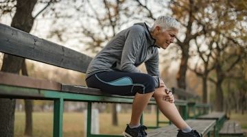 A grey-haired jogger crouches in pain, hand on her knee