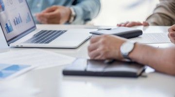 Closeup of hands around documents and a laptop in a business meeting