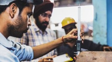 Three male employees in factory work together to ensure dimensions of pipe are correct