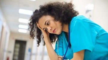 A nurse sits in deserted hospital hallway, looking worried