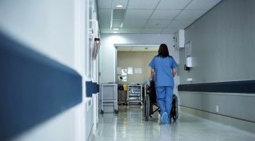 A long-term care worker pushes a resident in a wheelchair down the hall