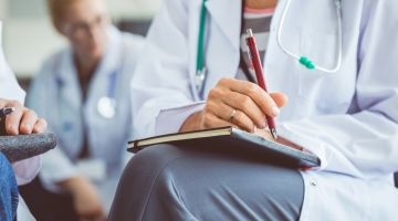 A group of physician's sitting in a room, prepared to take notes.