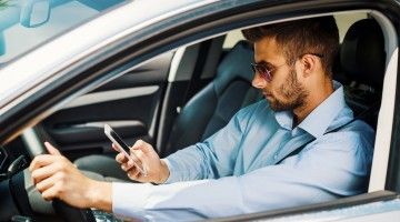 A young man behind the wheel of a car checks his smartphone