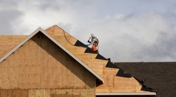 A lone roofing worker sits perched on top of a new being built