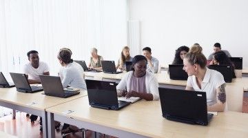 Diverse group of adults sit at laptops in training room