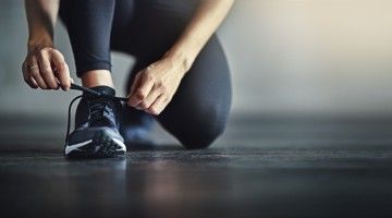 Close-up of a faceless jogger, lacing up her running shoes