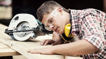 A young man cuts wood at a saw table