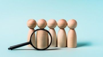 A magnifying glass is positioned in front of a row of five wooden figures