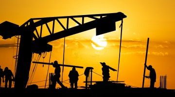 Silhouettes of construction workers against an orange sky