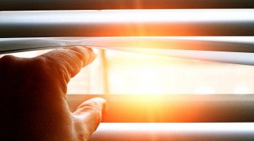 Close-up of fingers opening window blinds to let sun in
