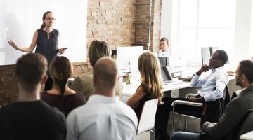 A roomful of working adults listen to a presenter