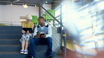 Two friendly colleagues sit on stairs, chatting 