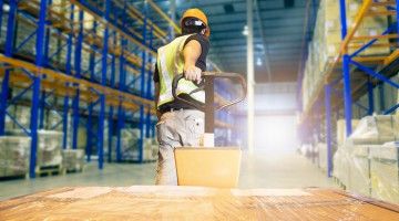 The back of a male worker, hauling a load in a warehouse setting