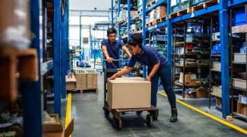 A man and a woman work together to push a trolley through a warehouse