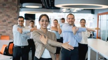 A group of office workers stand in rows, doing stretches