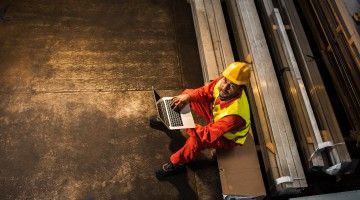 A helmeted worker sits on bench with laptop