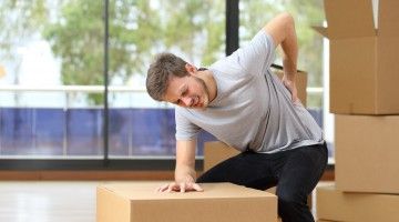 Male worker who is moving boxes holds his back in pain