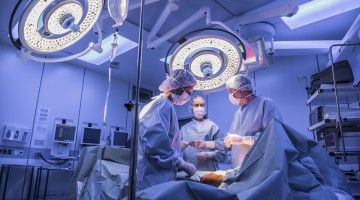 Three surgeons in operating room standing over patient