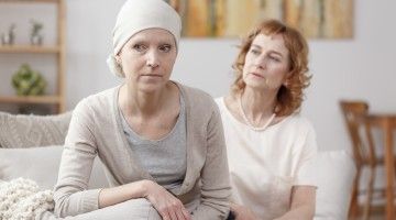 Two middle-aged women sit together, one wearing a head scarf indicating she has cancer