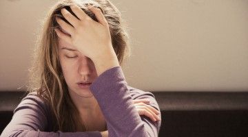 A young woman rests her head in her palm, eyes closed