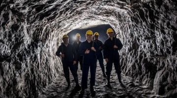A group of workers in yellow safety helmets stand in an underground mine