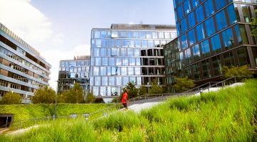 Man in red shirt jogs in a park adjacent to an office building