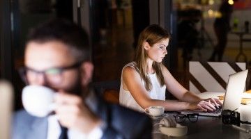 Two office workers sit at their computer workstations late into the night