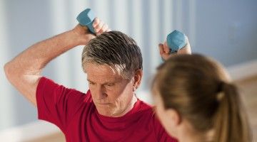 A mature man doing exercises with hand weights with help from a physiotherapist