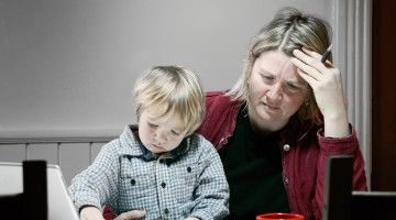 A woman, with toddler on her lap, stressfully goes through her bills