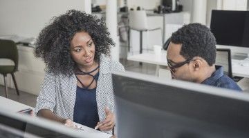 A supervisor talks one-on-one with a worker at a computer station