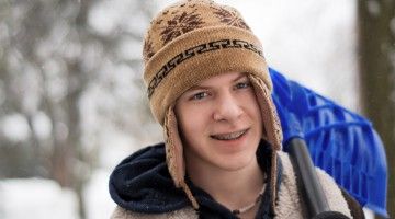 A teen hoisting a snow shovel over his shoulder