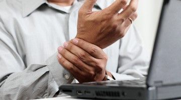 A man at the computer keyboard massages his wrist