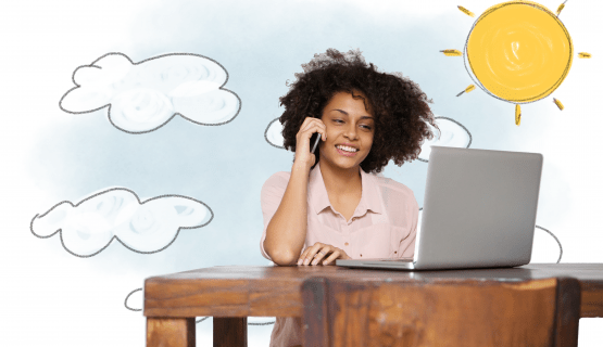 A smiling woman talks on the phone at her desk, with the sun shining behind her
