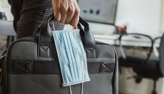 Close-up of a hand holding a surgical mask and a laptop case