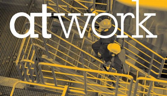 Yellow tinted picture of two people in safety helmets walking up a set of stairs. Superimposed white text reads: At Work