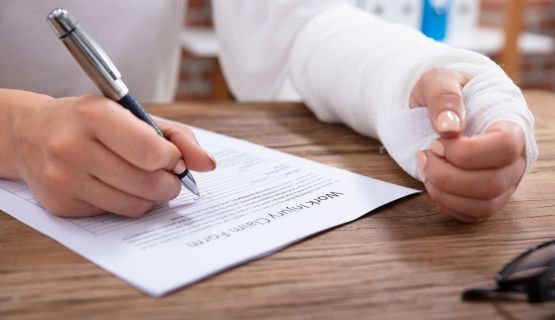 A woman with a bandaged left arm fills out injury claim form