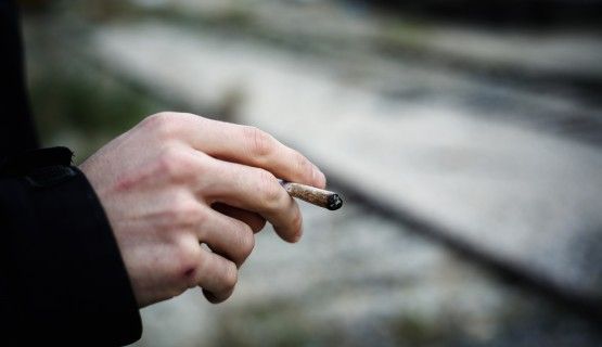 A close-up of a man's hand, holding a joint
