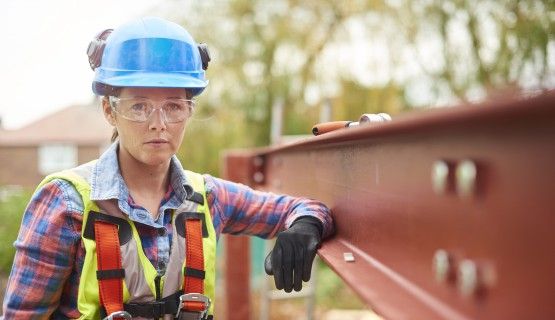 A female construction worker stands next to a steel girder