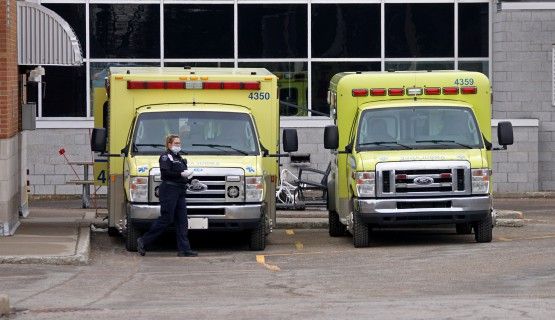A paramedic wearing a face mask stands next to two ambulances