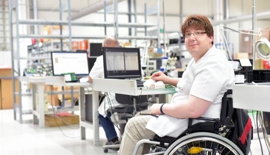 A computer technician who uses a wheelchair works at his station
