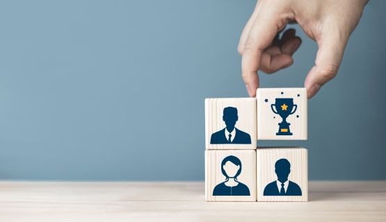 Blocks with workers' silhouettes, one with a trophy is picked up by a hand.