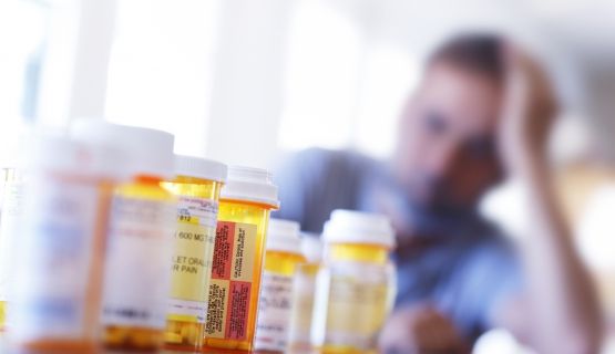 A man with his head in his hand looks at a row of empty pill bottles