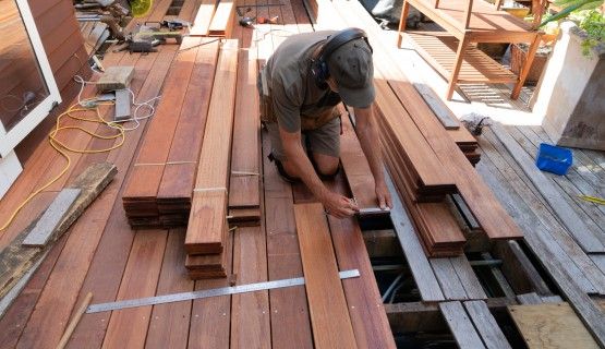 A man kneels as he works with decking boards on a patio