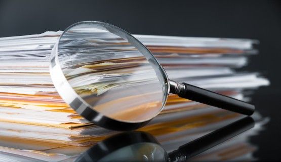 Magnifying glass against stack of research papers Thumbnail