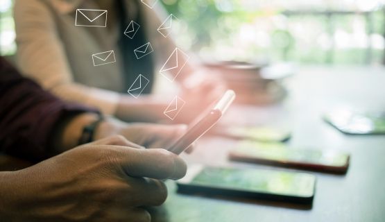 A close up of smart phones on a surface or held in people's hands, with email icons floating above them