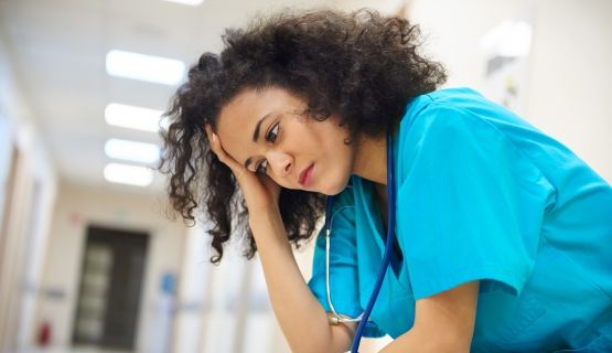 A nurse sits in deserted hospital hallway, looking worried