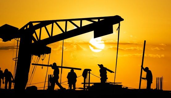 Silhouettes of construction workers against an orange sky