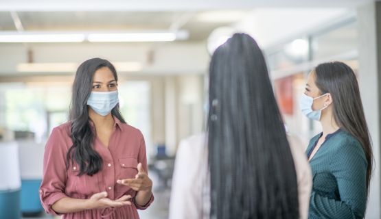 Three women wearing masks talking to each other at work