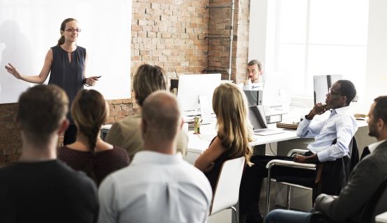 A roomful of working adults listen to a presenter