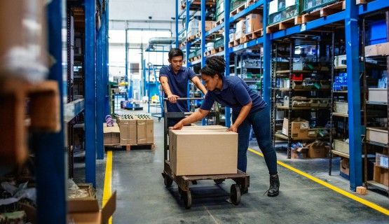 A man and a woman work together to push a trolley through a warehouse